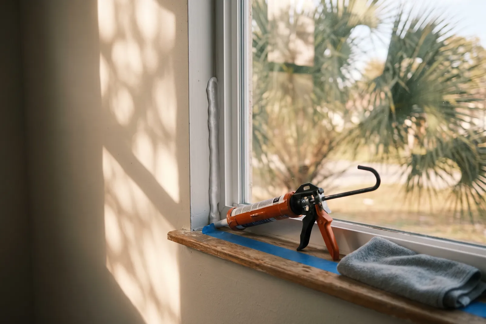 Fresh bead of white sealant being applied along a window frame