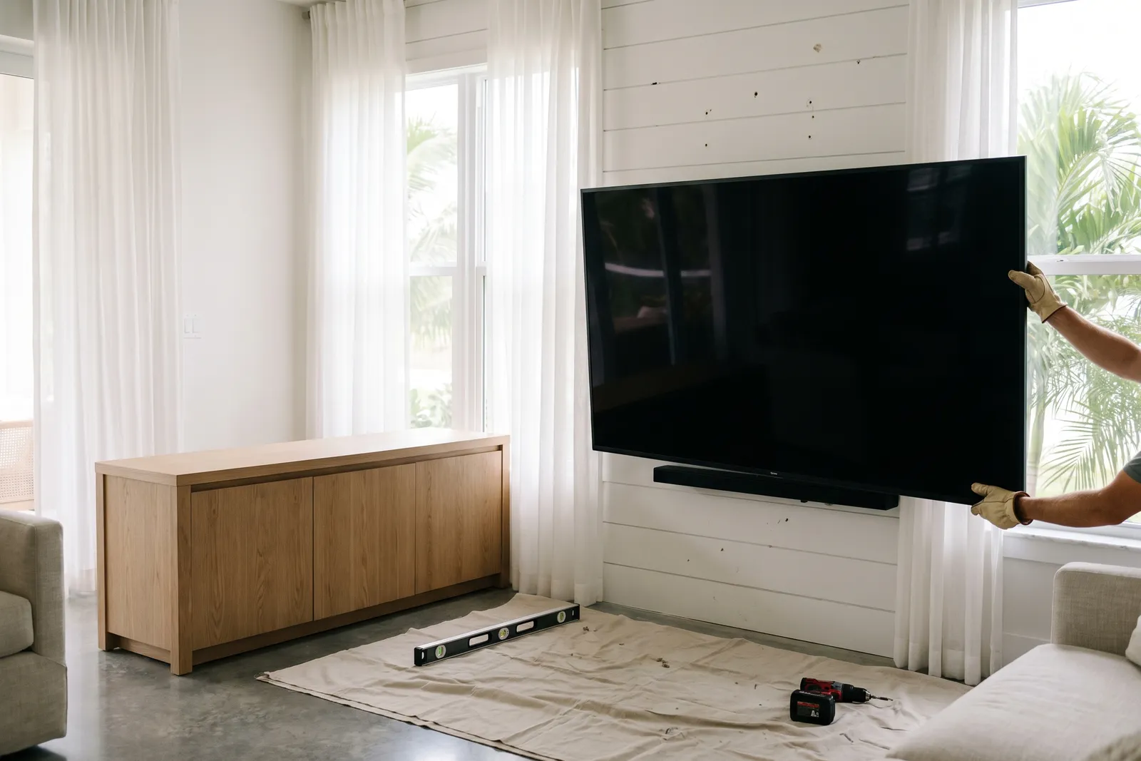 Gloved hands steadying a TV onto its wall mount